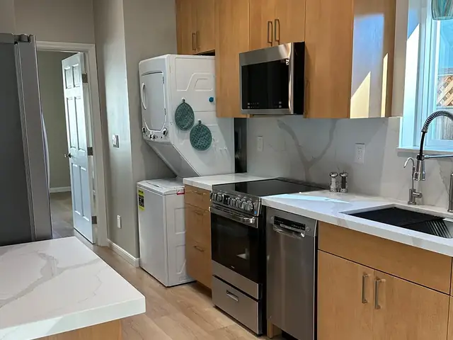 Finished ADU kitchen with quartz counters, stainless appliances and a stacked washer and dryer