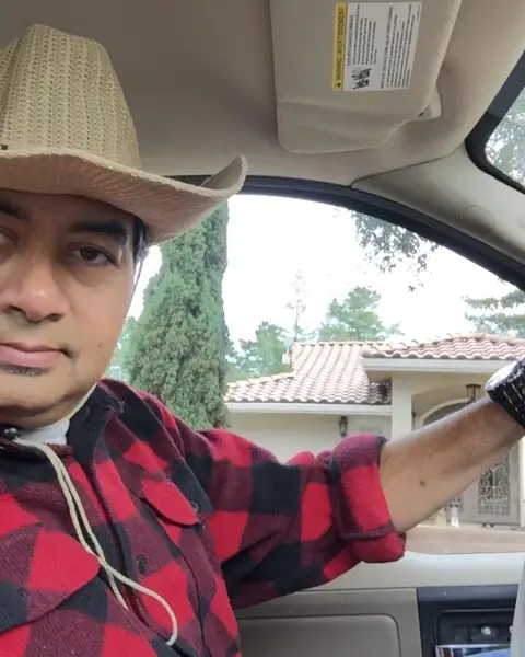 Kamal Hyder in a cowboy hat, smiling from the driver's seat of his truck